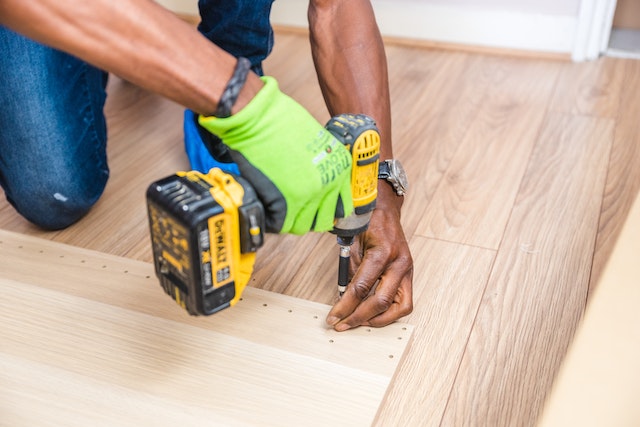 person in green work gloves using electric drill on a piece of wood